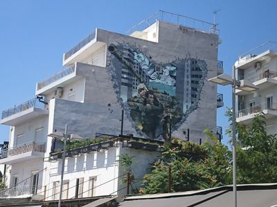 Façade blanche d'un immeuble typique polykatoikia à Athènes avec une grande fresque de street art colorée sous un ciel bleu azur.