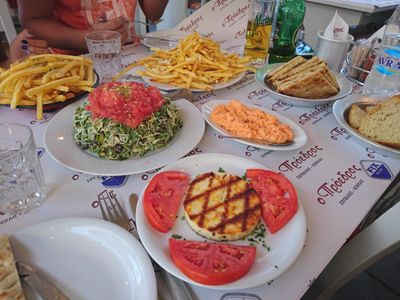 Table de taverne grecque traditionnelle garnie de spécialités locales, fromage grillé, frites, salade de tomates et pain frais à Athènes.