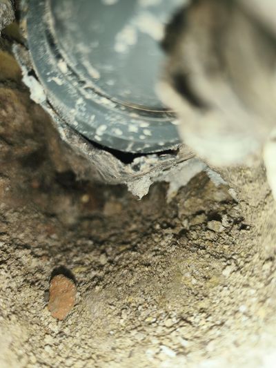Extreme close-up inside a wall cavity exposing a failed plumbing connection, showing a visible gap where a newer grey plastic evacuation pipe was improperly joined to an older cast-iron system.